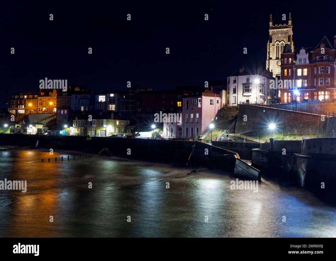 Guardando verso la chiesa di Cromer e le strade marittime Cromer Pier nel Nord Norfolk di notte in una fredda serata autunnale con una calda luce dagli edifici illuminati. Foto Stock