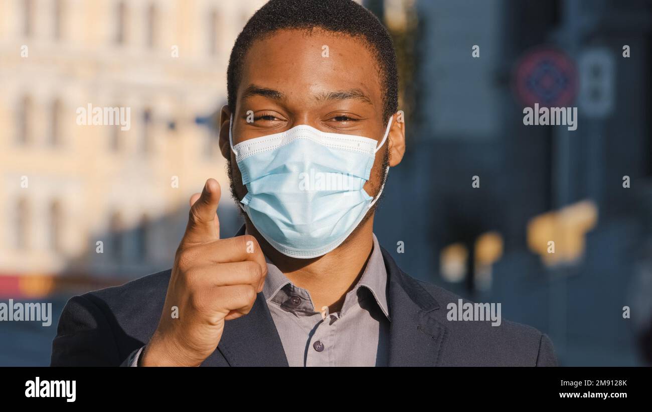 Uomo d'affari afro americano uomo etnico maschio ragazzo in maschera medica che punta con il dito hey si è d'accordo mostrare numero uno gesto di supporto scelta Foto Stock
