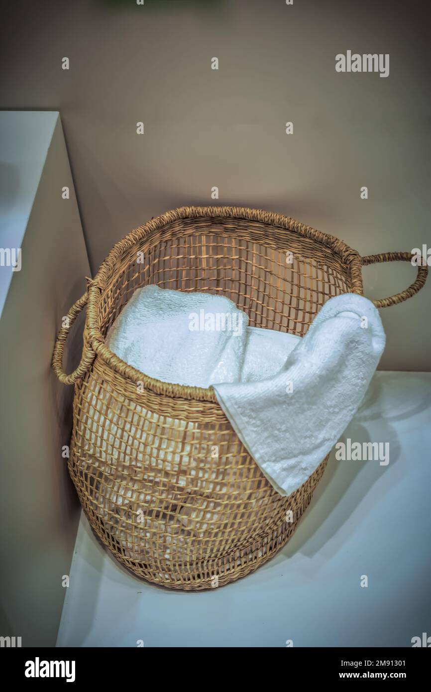 Un cesto di vimini pieno di asciugamani bianchi sul pavimento Foto Stock