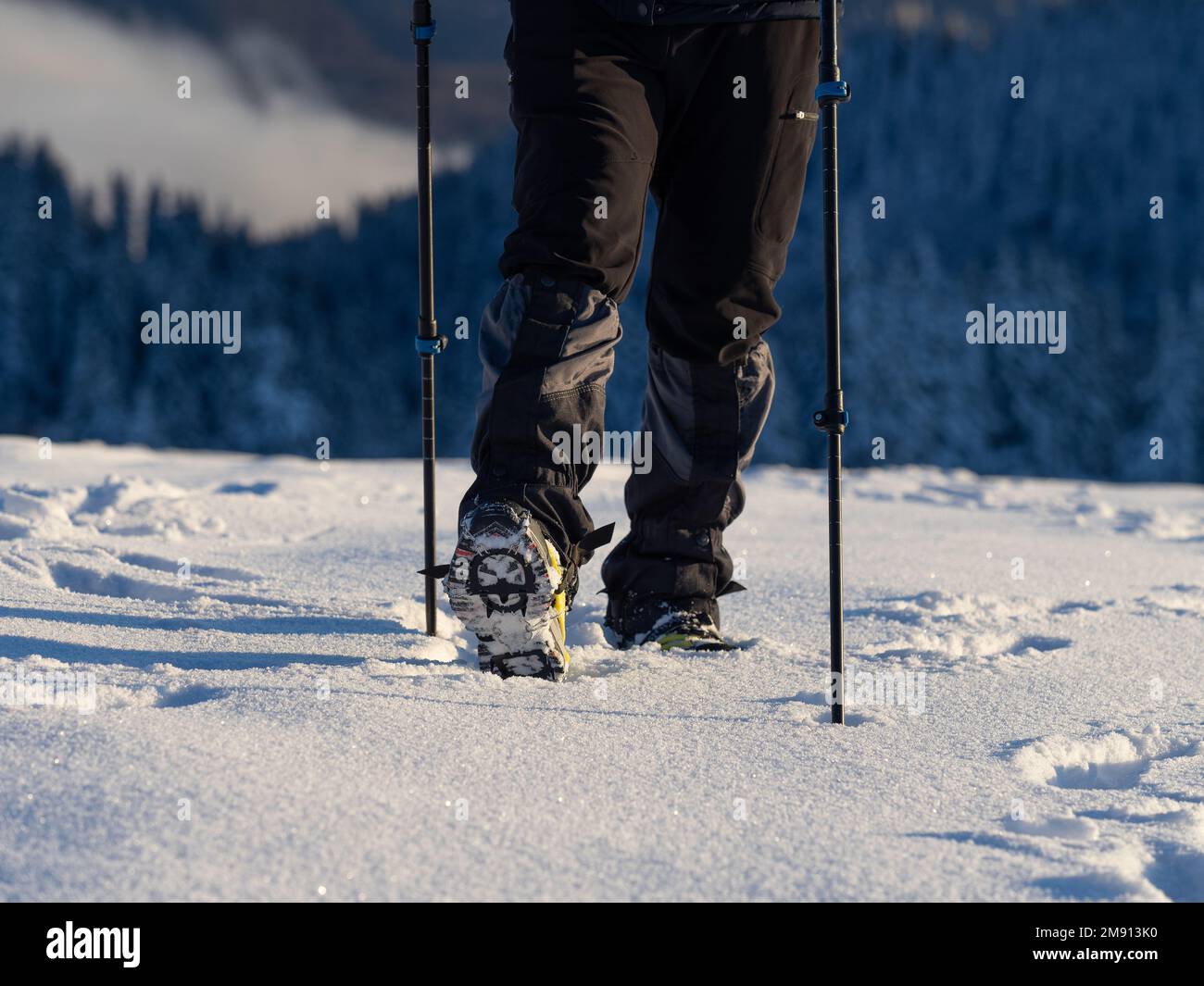 Primo piano di un uomo che si arrampica su una montagna coperta di neve, in scarponi con pattini. Trekking invernale all'aperto Foto Stock