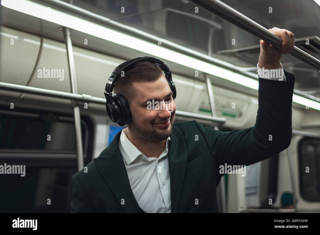 uomo giovane uomo uomo caucasico passeggero una persona positivamente allegro ascolta la musica in cuffie, sorride e andare in metropolitana di trasporto al mattino. abbonamento concettuale alla musica. Foto Stock
