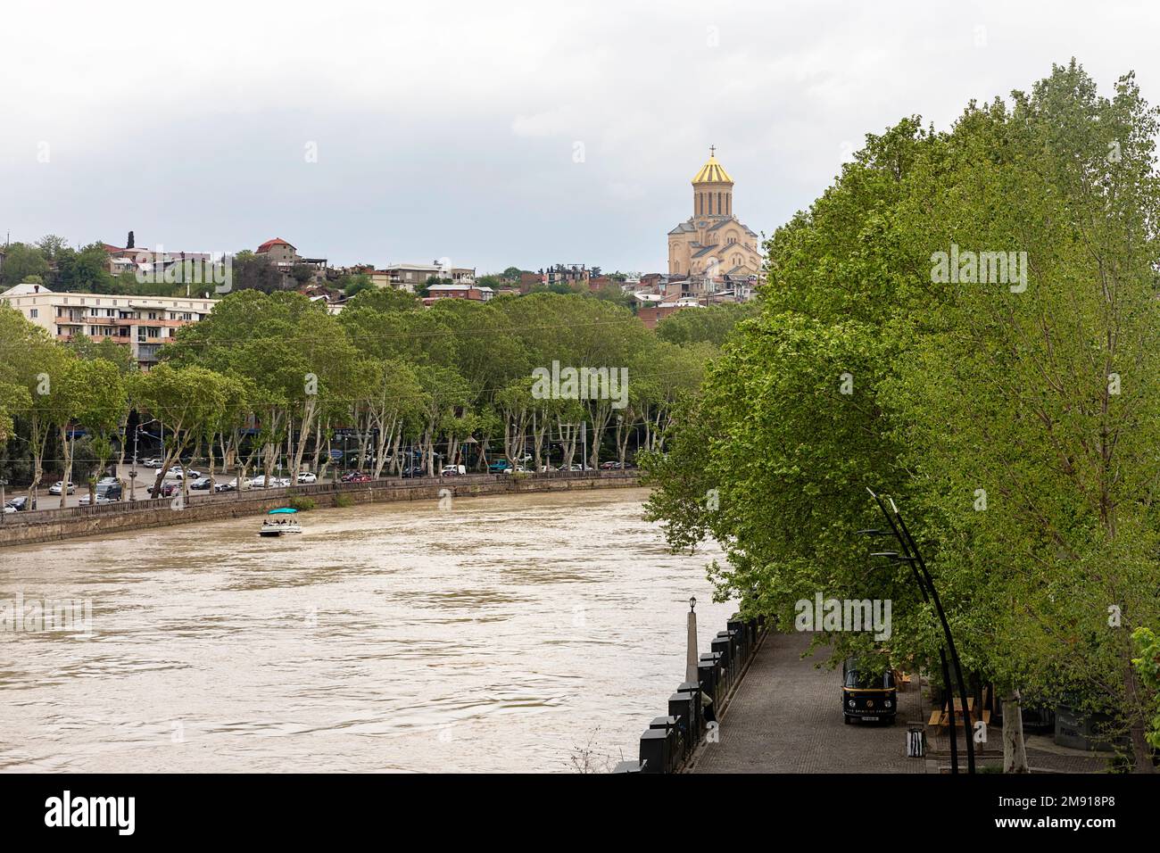 Una barca sul fiume Kura e vicolo con traffico a Tbilisi, con la chiesa della Santissima Trinità sullo sfondo, Georgia, Caucaso Foto Stock