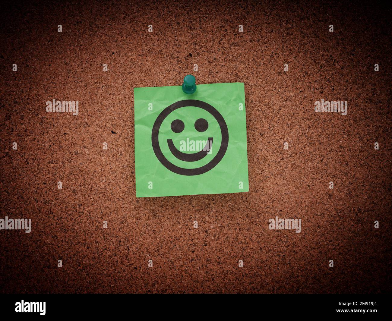 Una nota di carta verde stropicciata con il volto sorridente fissato a un corkboard. Primo piano. Foto Stock
