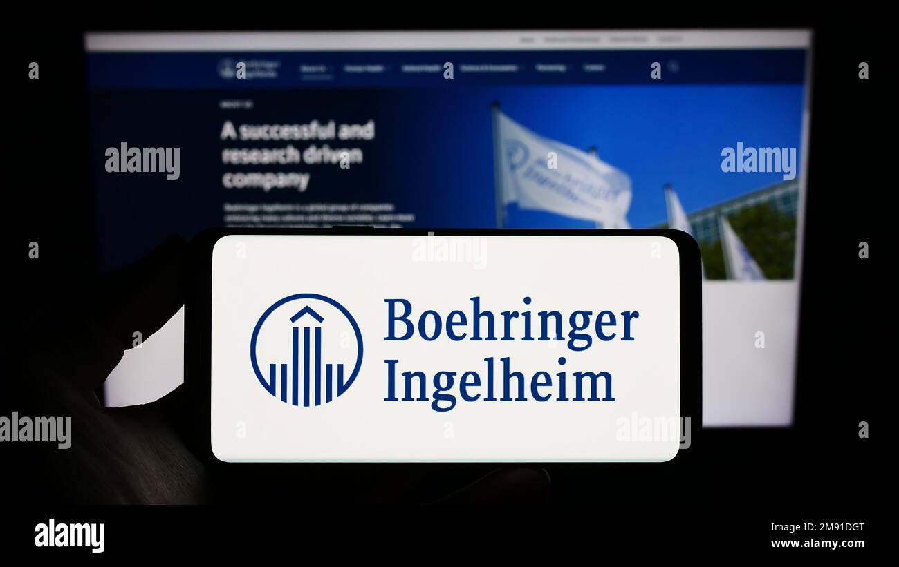 Persona che tiene uno smartphone con il logo della società farmaceutica Boehringer Ingelheim sullo schermo di fronte al sito web. Messa a fuoco sul display del telefono. Foto Stock