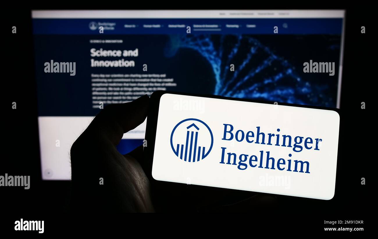 Persona che tiene il cellulare con il logo della società farmaceutica Boehringer Ingelheim sullo schermo di fronte al sito web aziendale. Messa a fuoco sul display del telefono. Foto Stock