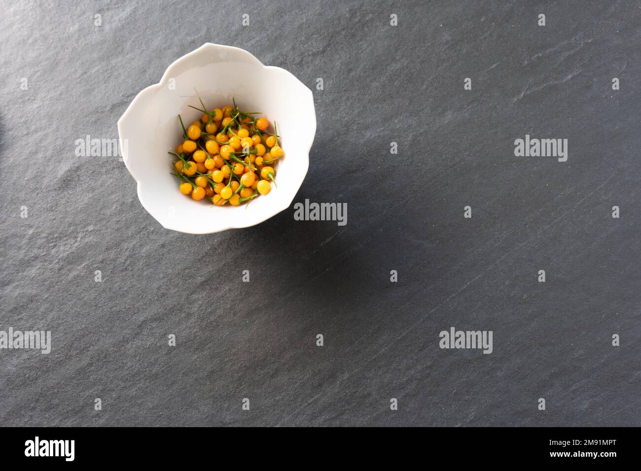 Una ciotola bianca di rari peperoni aji charapita su uno sfondo grigio ardesia con spazio copia; fotografia di cibo Foto Stock