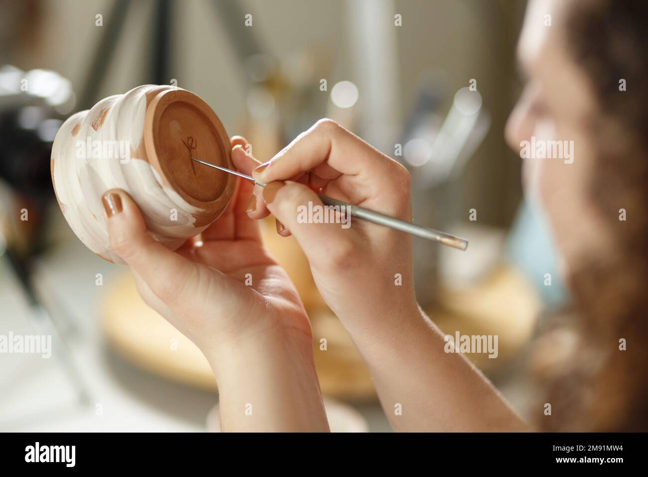 Giovane donna che fa ceramica al chiuso in studio creativo artigianale concetto seduta a tavola utilizzando strumento di modellazione creazione di dettagli sulla tazza. Foto Stock