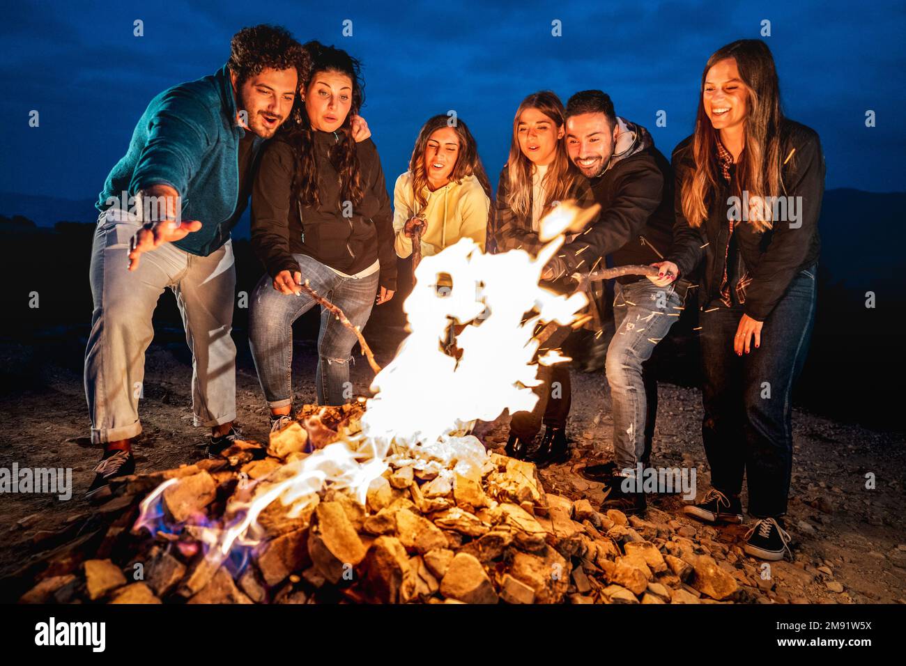 Giovani che si divertono insieme di notte festa intorno falò - Wanderlust stile di vita concetto con amici felici viaggiatore che si fanno caldi Foto Stock