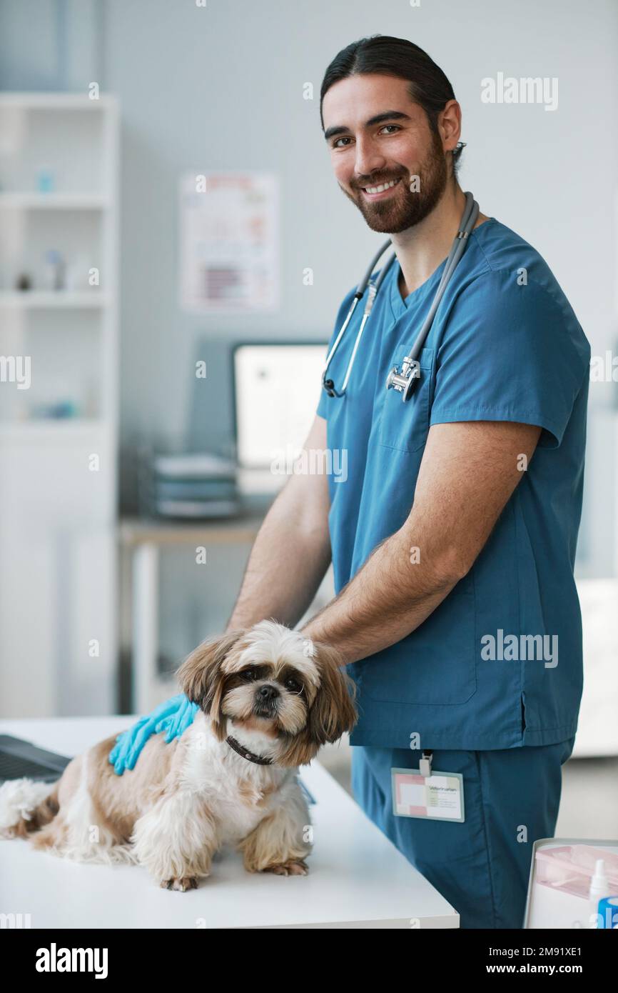 Giovane medico veterinario maschio in uniforme e guanti in piedi da tavolo  medico con yorkshire terrier e guardando la macchina fotografica durante il  check-up Foto stock - Alamy