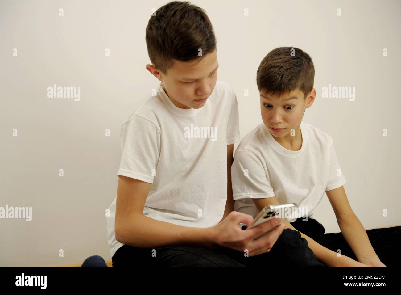 Due ragazzi adolescenti guardare il telefono con interesse uno di loro ha  aperto gli occhi e ha sollevato le sue sopracciglia qualcosa di  interessante bianco t-shirt adolescenti online apprendimento social network  giochi