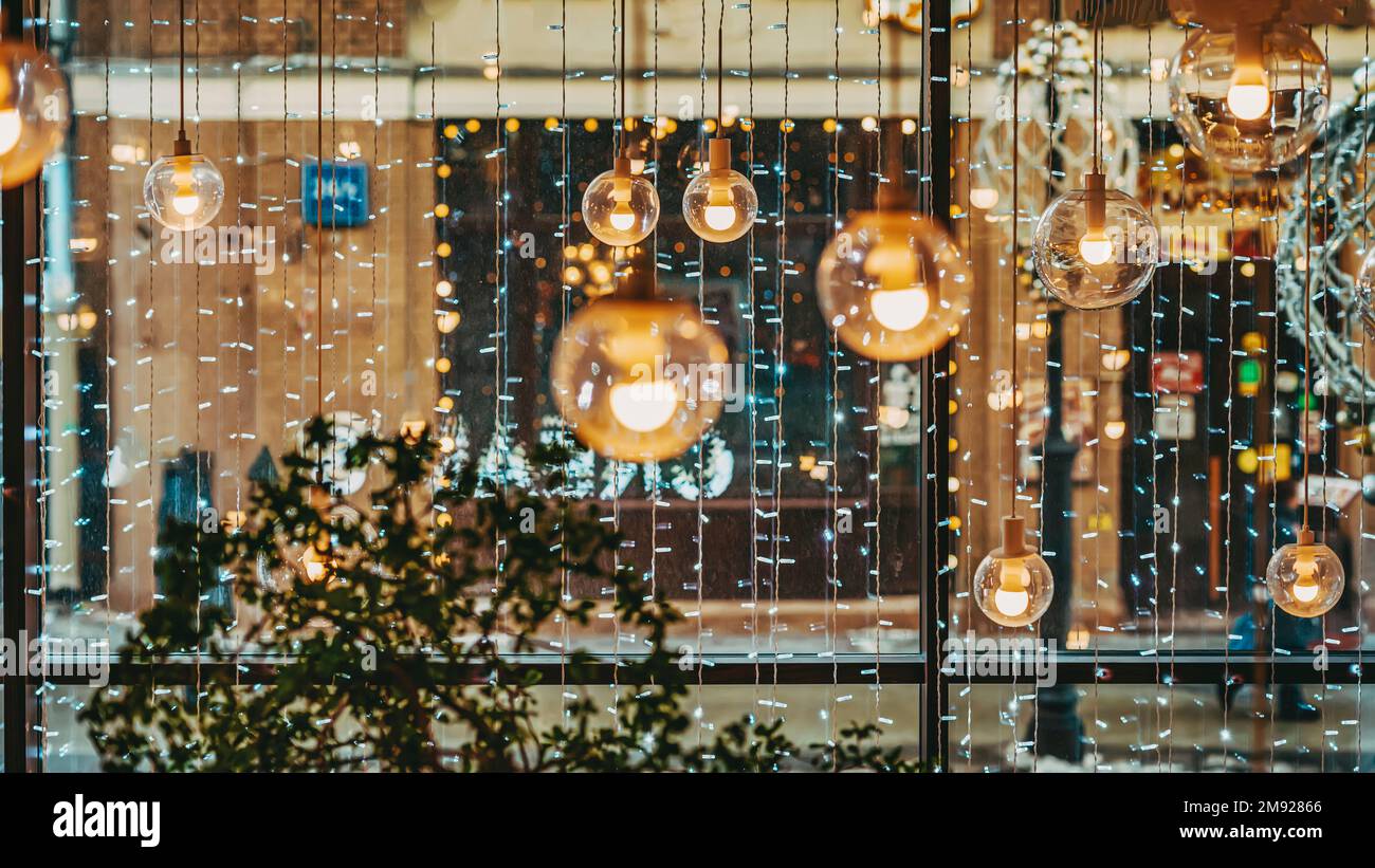 Astratto sfondo sfocato con grande finestra panoramica. Decorazioni natalizie, luci ghirlande, lampade, lanterne Foto Stock