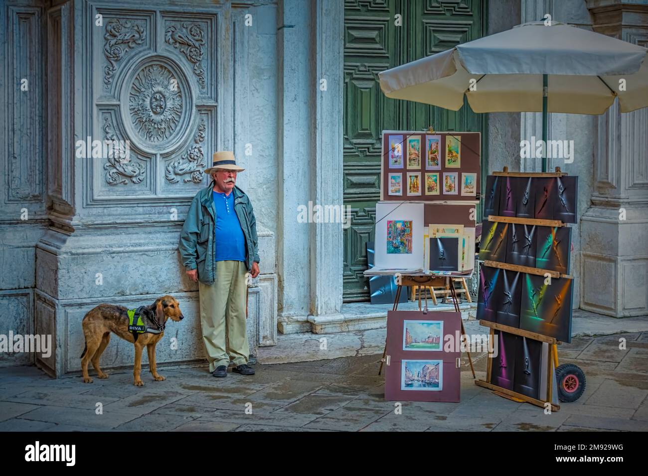 Un venditore d'arte, accompagnato dal suo cane, vende i suoi dipinti presso lo stand di vendita di campo San Moisè a Venezia Foto Stock