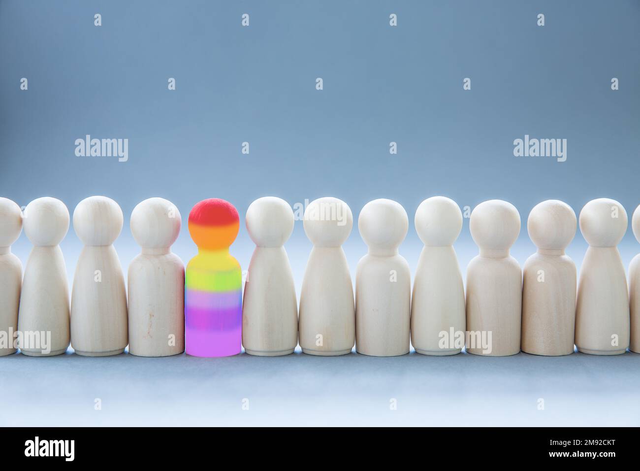 Una fila di figure umane con un singolo individuo che si distingue dal resto che rappresenta l'individualità e l'inclusione nella comunità come una persona gay Foto Stock
