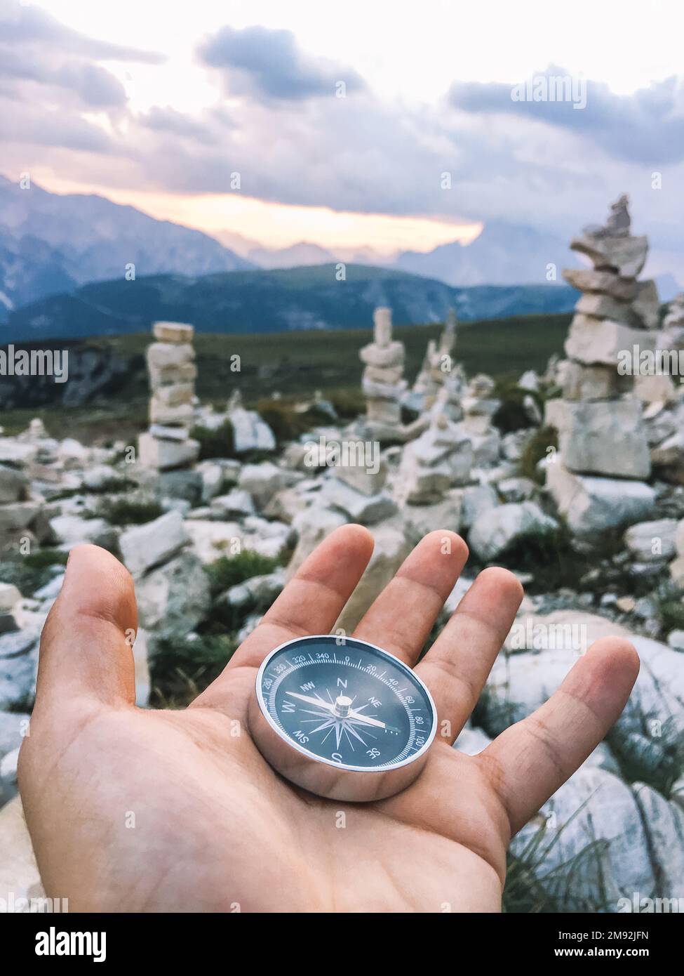 Bussola tenuta a mano in un paesaggio montano. Il viaggiatore che realizza i suoi sogni in cima a una montagna con cairns in pietra sullo sfondo. Concep Foto Stock