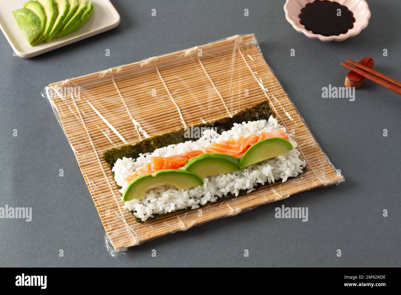 Da sopra di sushi costituito da salmone di riso di alghe e avocado posto su tappeto di rotolamento vicino a bastoncini e salsa di soia Foto Stock