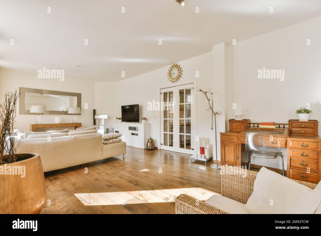 Design interno di una spaziosa e moderna zona soggiorno con pareti bianche pavimento laminato grande divano TV specchio scrivania con sedia in vetro e poltrona nelle giornate di sole Foto Stock