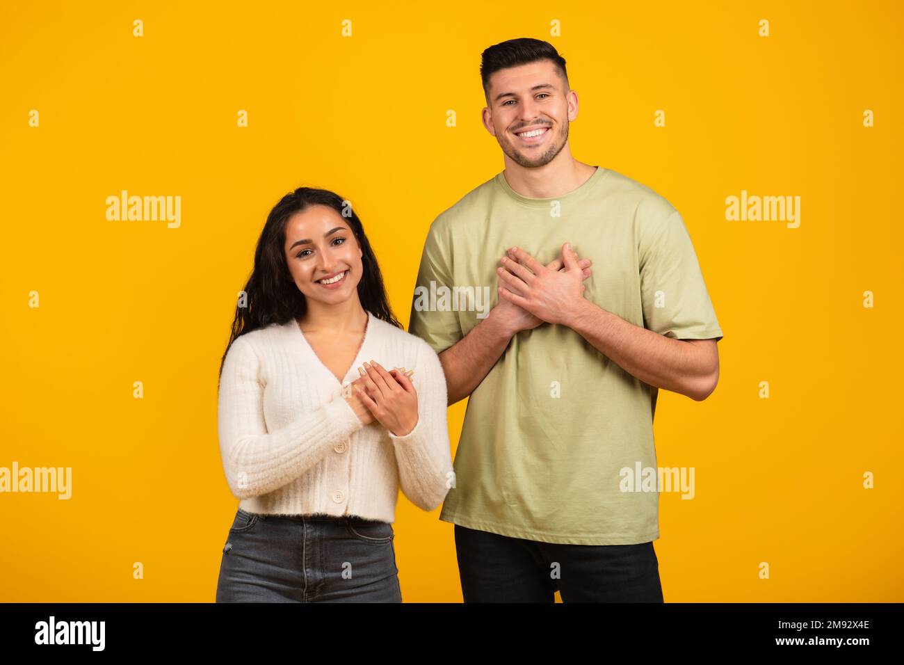 Sorridente ragazzo e donna araba millenaria in abiti casual premere le mani al petto, dire grazie Foto Stock