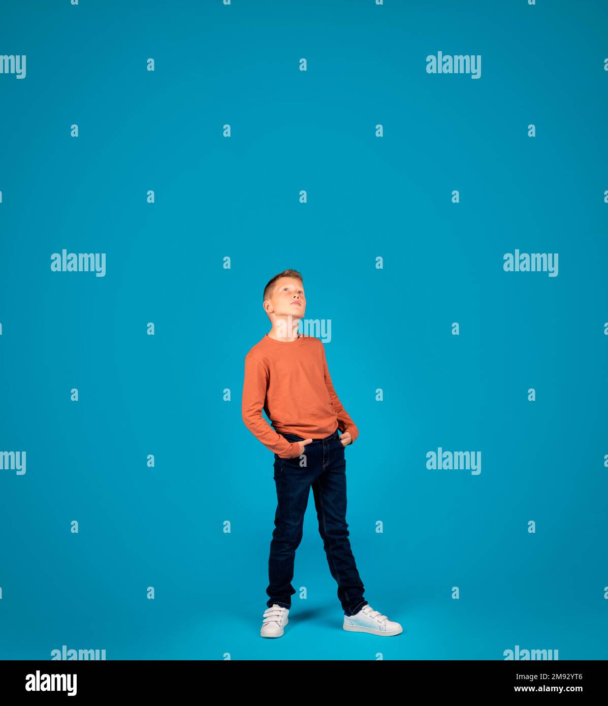 Curioso ragazzo Preteen che guarda in su con interesse mentre in piedi su sfondo blu Foto Stock