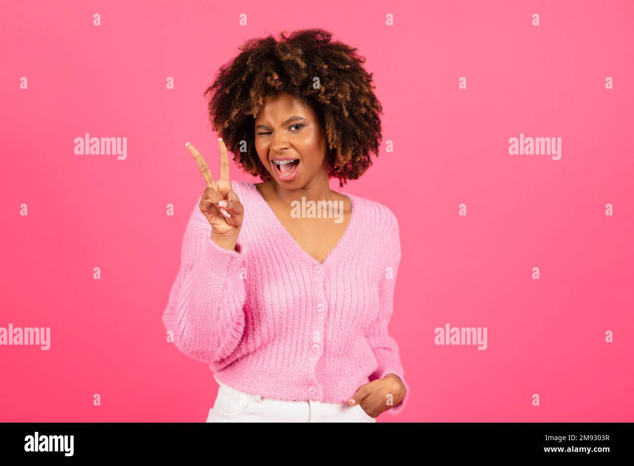Allegro giovane donna afroamericana in verricelli casual, mostrare segno di pace con la mano Foto Stock