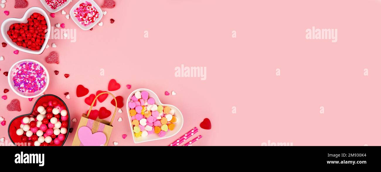 San Valentino angolo caramelle bordo con una varietà di dolci. Vista dall'alto su uno sfondo di striscione di carta rosa con spazio per la copia. Foto Stock