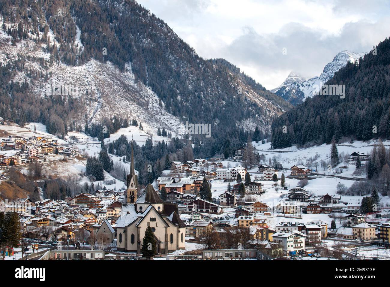 Neve fresca del mattino nelle Dolomiti dietro la Chiesa di San Vigilio e altri edifici del villaggio, Moena, Italia, gennaio 2023 Foto Stock