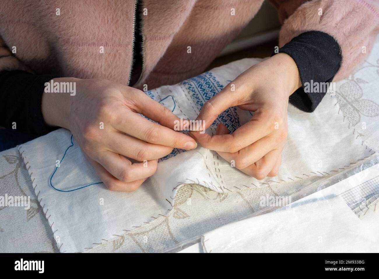 Primo piano delle mani di una donna che cucia una maglietta nazionale Ucraina ricamata Foto Stock