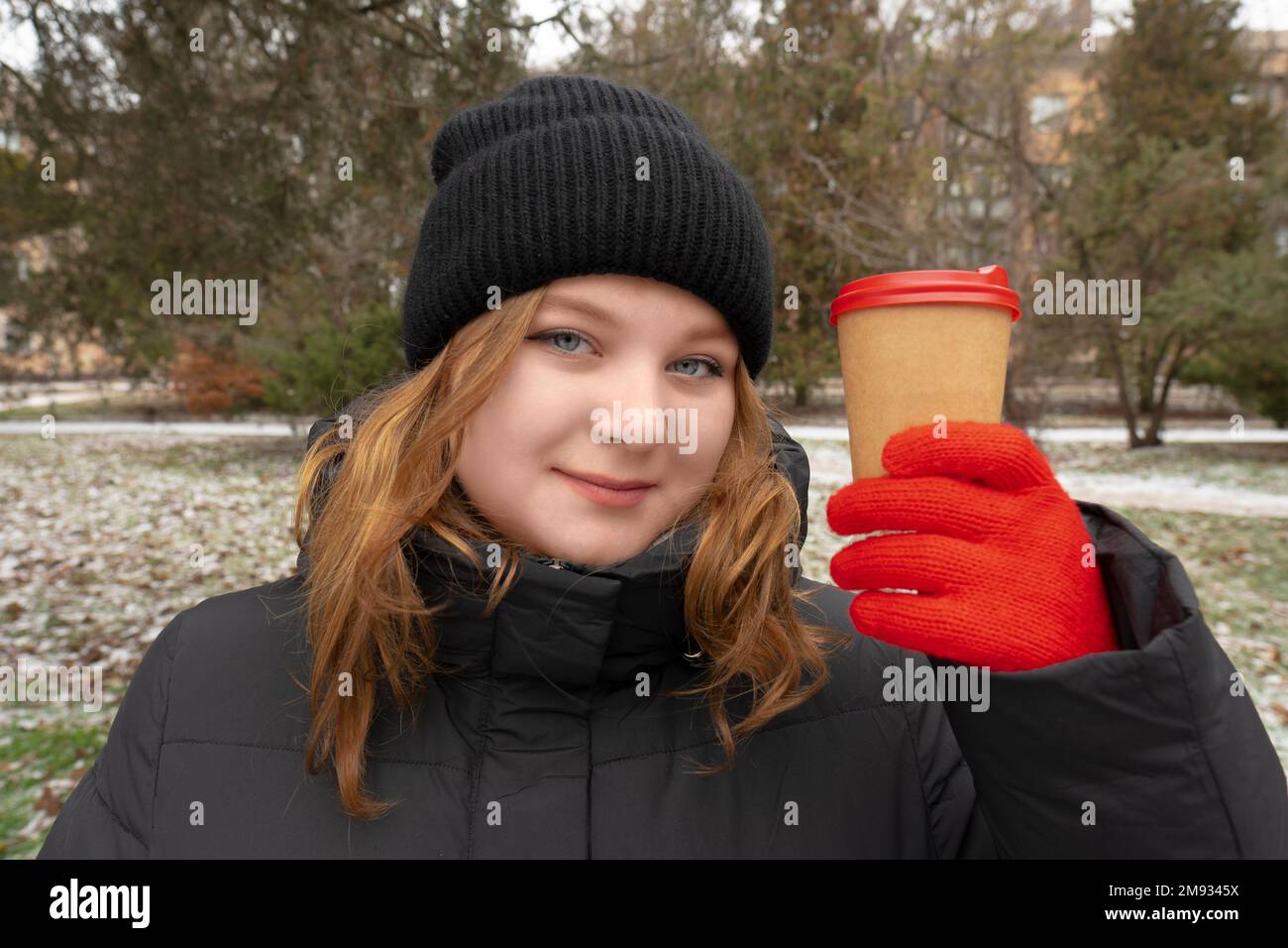Inverno. Clima freddo. Parco cittadino. La ragazza tiene in mano una tazza di caffè. Stile di vita. Passeggiate all'aperto Foto Stock