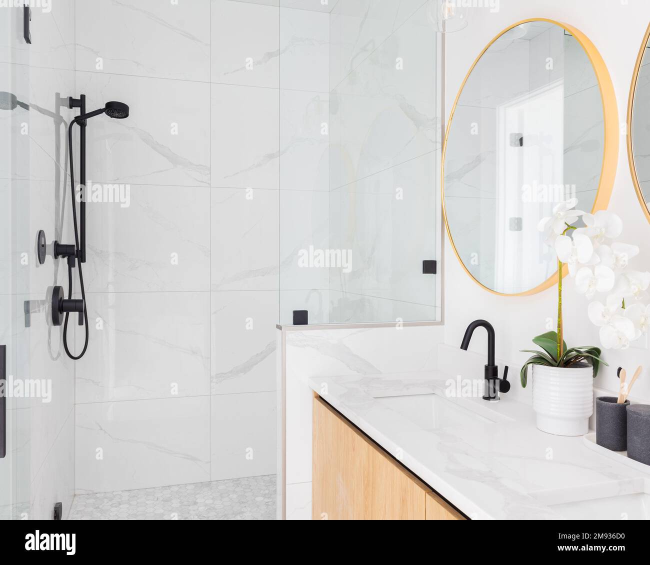 Un lussuoso bagno con armadio galleggiante in legno, ripiano in marmo, specchi dorati e cabina doccia piastrellata in marmo. Foto Stock