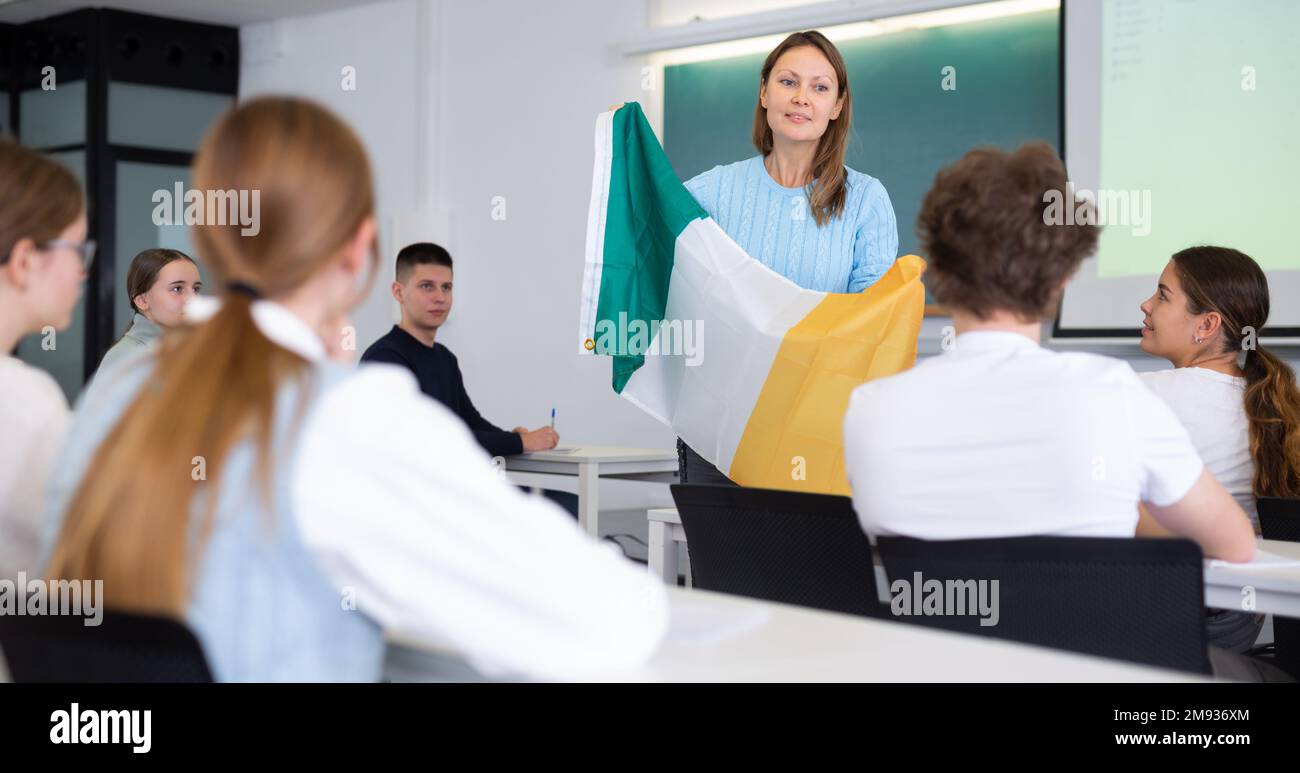 L'insegnante delle scuole superiori racconta agli studenti l'Irlanda e tiene in mano una bandiera irlandese. Foto Stock