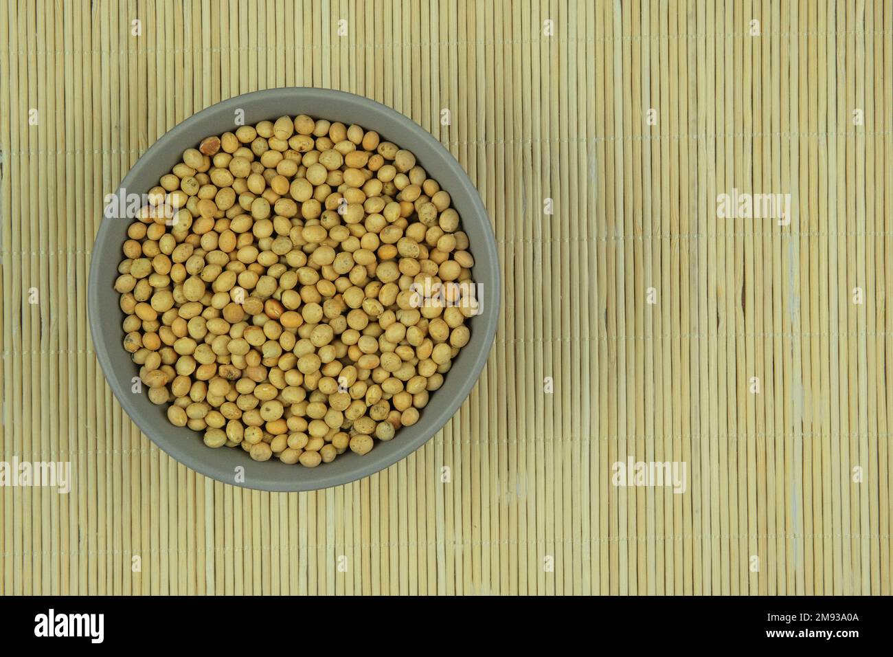 I fagioli di soia in ciotola su uno sfondo di paglia. Impulso proteico che viene essiccato e poi imbevuto e cotto prima di mangiare. Prodotto vegetariano. Vista dall'alto. Foto Stock