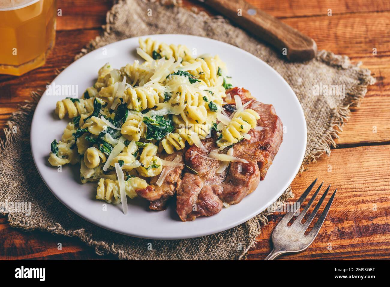 Bistecca al collo di maiale e pasta cremosa con spinaci e timo Guarnito con parmigiano grattugiato su piatto bianco Foto Stock