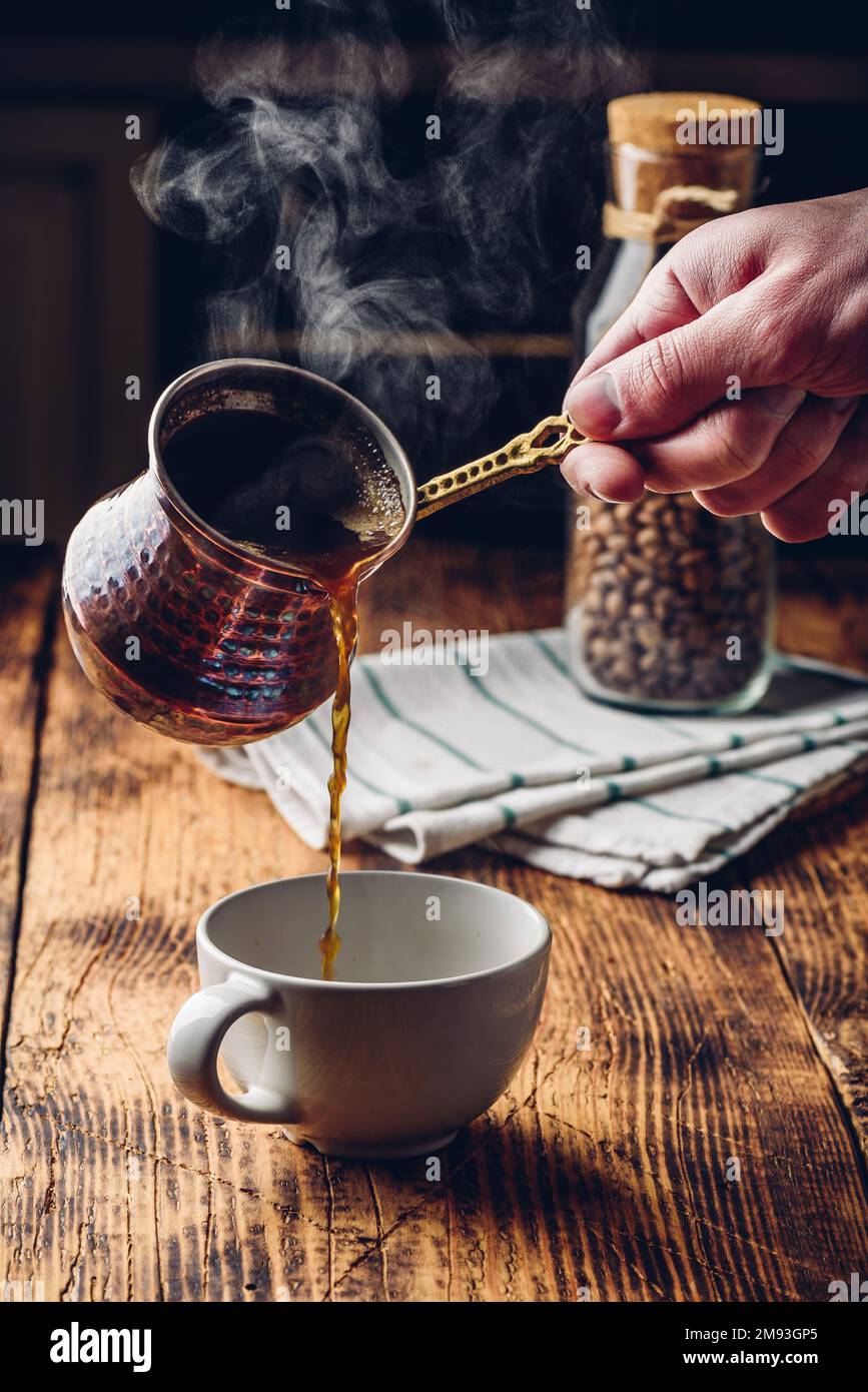 Versare il caffè turco in una tazza bianca. Vasetto di chicchi di caffè tostati su sfondo Foto Stock