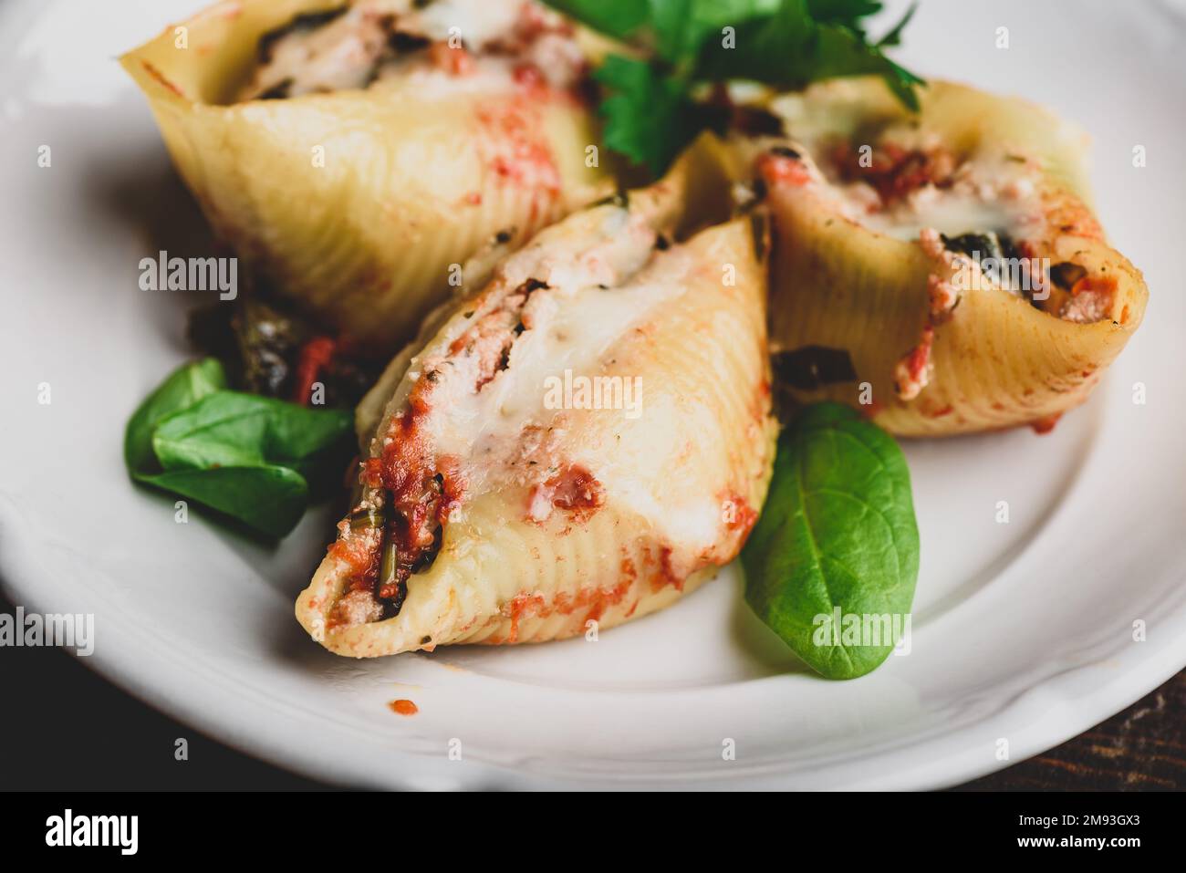 Conchiglie di jumbo al forno farcite con manzo macinato, spinaci e formaggio su piatto bianco Foto Stock