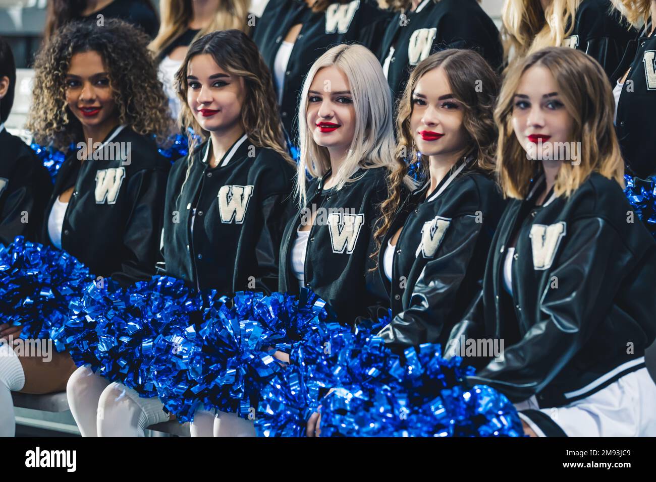 Cinque cheerleaders seduti tenendo pom blu e guardando la macchina fotografica. Concetto sportivo. Foto di alta qualità Foto Stock