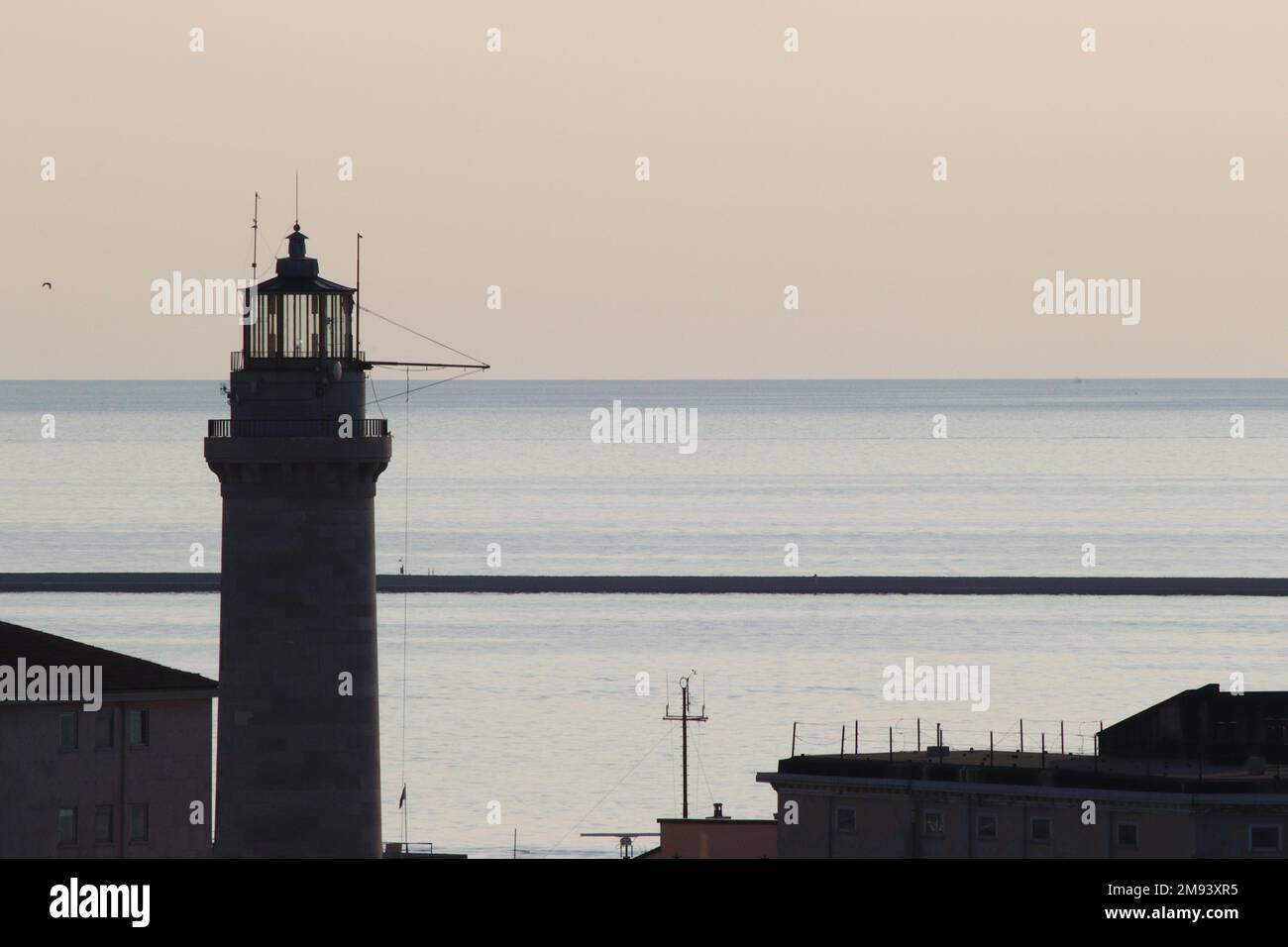 L'esordio della luce notturna sul porto di Trieste e sul faro della Lanterna di Trieste, trasformando elementi visibili in silhouette. Foto Stock