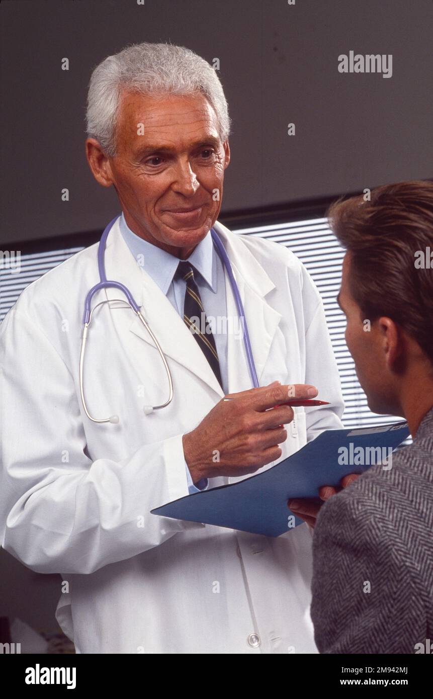 Primo piano di un vecchio medico di sesso maschile che va oltre le cartelle cliniche con un paziente di sesso maschile Foto Stock