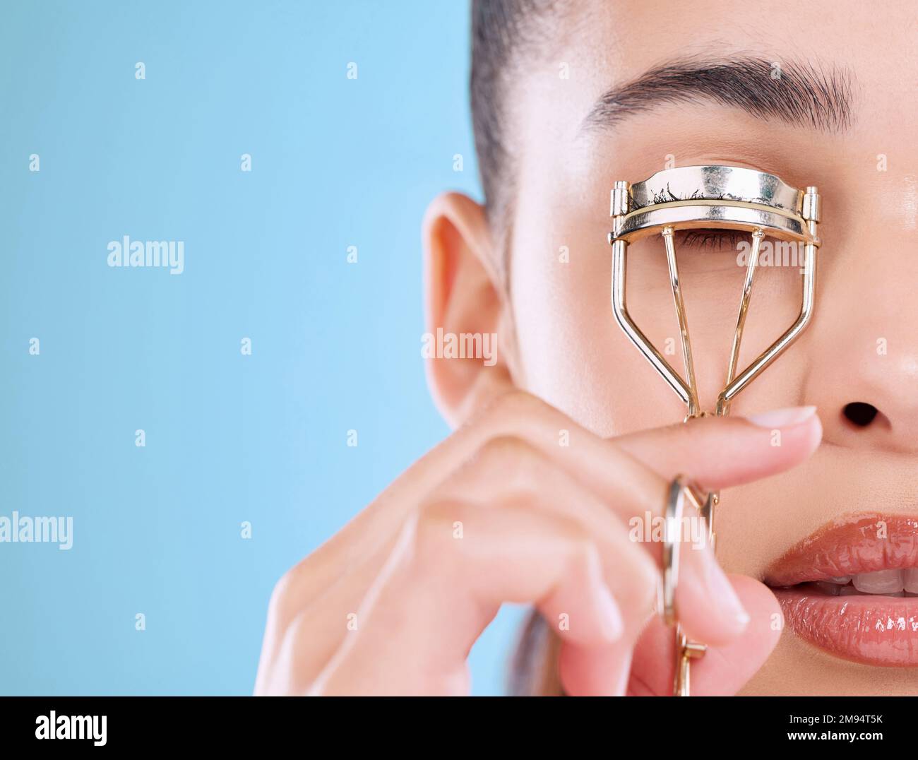 Faccia una dichiarazione con i vostri lashes. Studio shot di una giovane donna attraente utilizzando un arricciacapelli ciglia su uno sfondo blu. Foto Stock