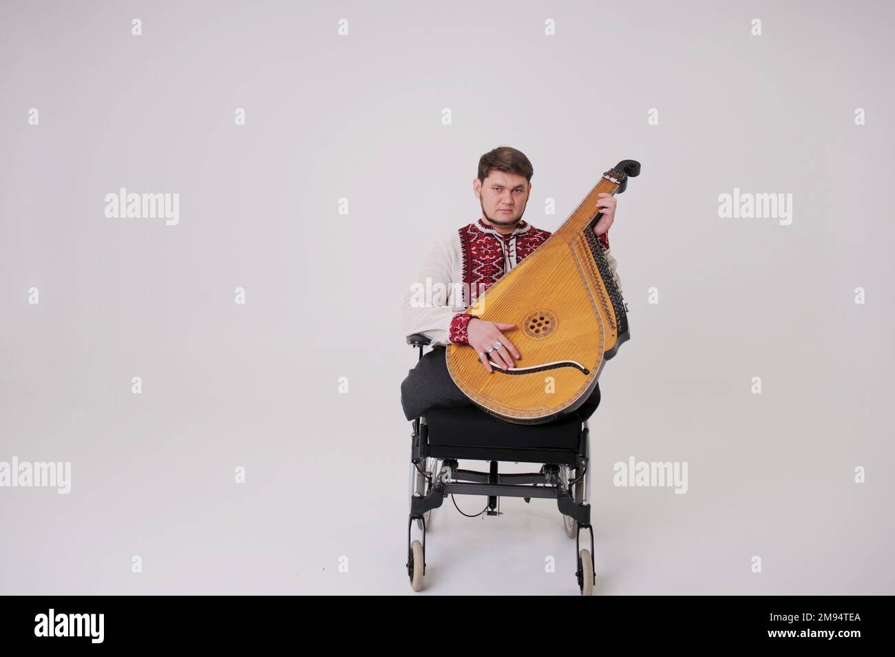 Bel giovane uomo con lo strumento musicale kobza in mano siede su sfondo bianco veterano di guerra vestito in camicia Ucraina ricamata simboli nazionali di Ucraina vyshyvanka Play harp Cossack ucraino Foto Stock