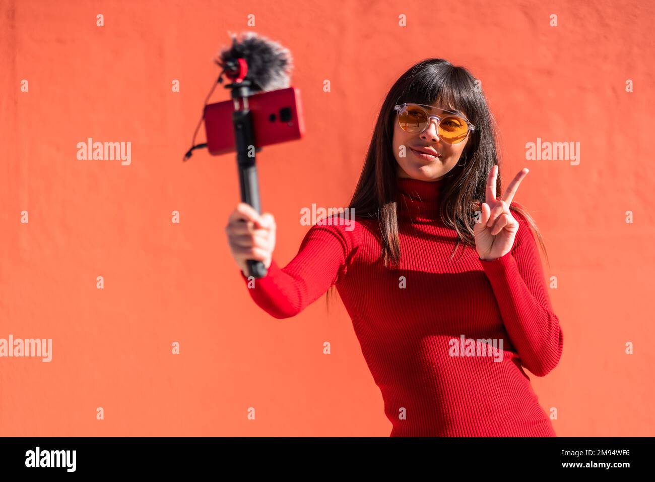 Brunette ragazza fare il segno di vittoria registrazione di un video blog con il cellulare Foto Stock