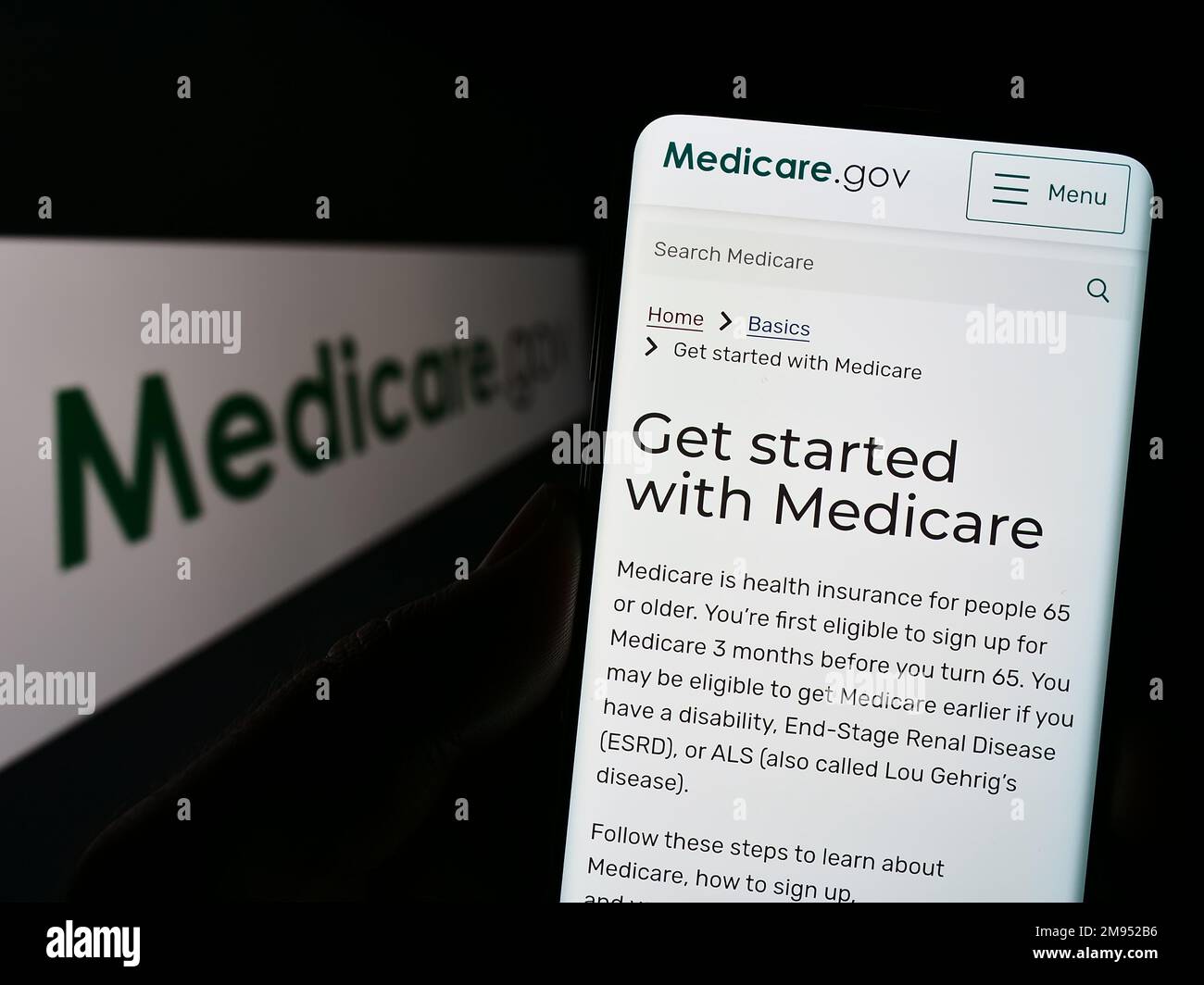 Persona che tiene il cellulare con il sito web del programma di assicurazione sanitaria americana Medicare sullo schermo di fronte al logo. Messa a fuoco al centro del display del telefono. Foto Stock