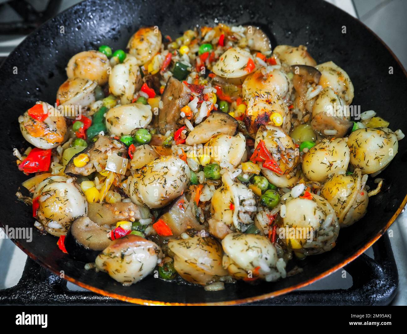 gnocchi con riso, piselli, mais, peperoni e melanzane vengono fritti in una padella in cucina per dei cibi squisiti Foto Stock