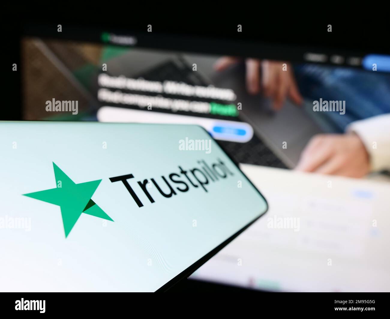 Smartphone con il logo della piattaforma di revisione società Trustpilot Group plc sullo schermo di fronte al sito Web aziendale. Messa a fuoco a sinistra del display del telefono. Foto Stock