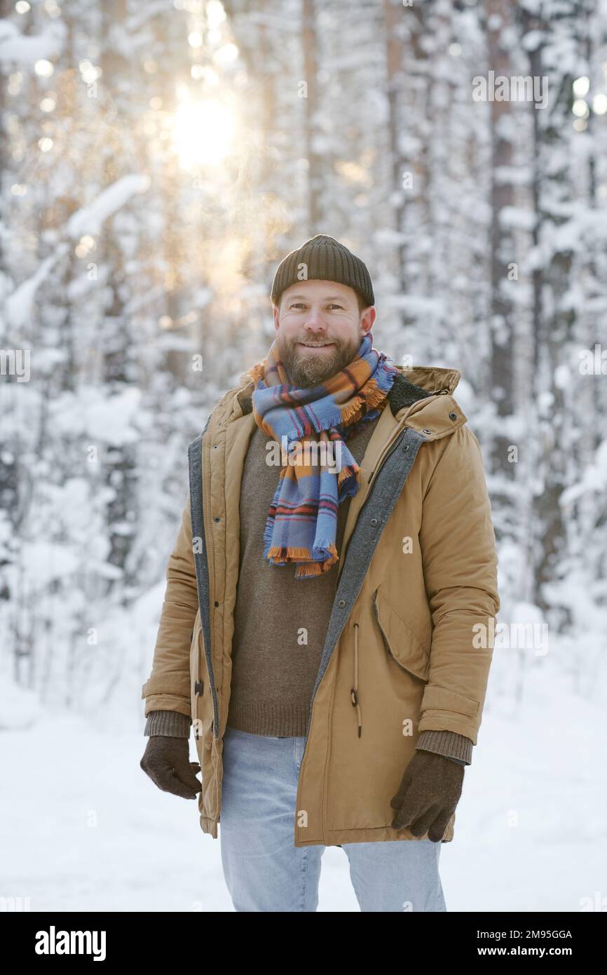 Ritratto di giovane uomo felice sorridente alla macchina fotografica mentre cammina nella foresta in inverno Foto Stock
