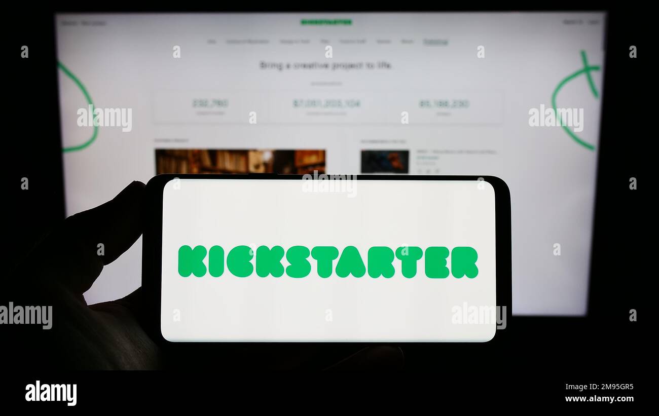 Persona che tiene in mano uno smartphone con il logo della piattaforma di crowdfunding statunitense Kickstarter PBC sullo schermo davanti al sito Web. Messa a fuoco sul display del telefono. Foto Stock