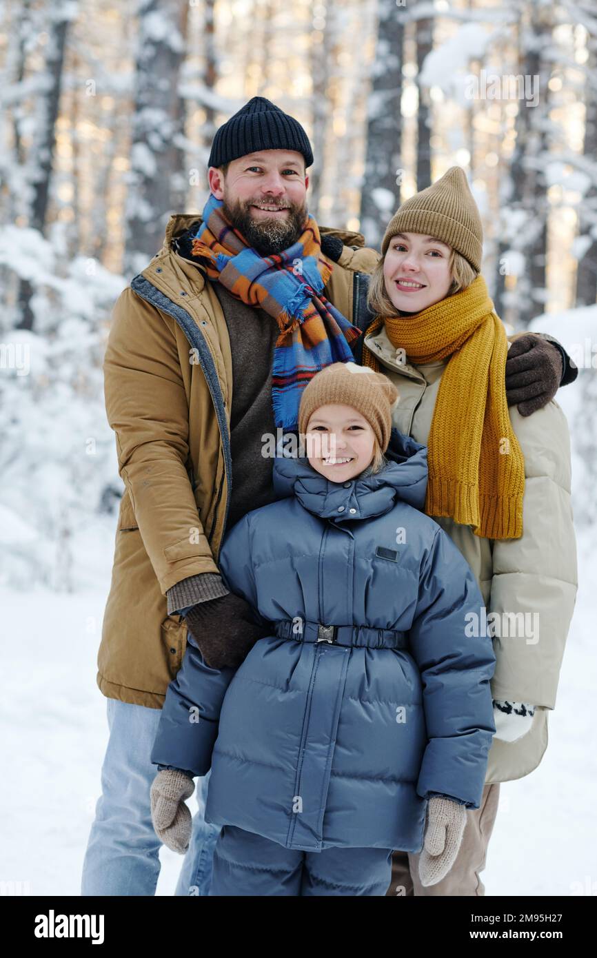 Ritratto di famiglia felice con bambino abbracciando e sorridendo alla macchina fotografica durante la loro passeggiata in inverno Foto Stock