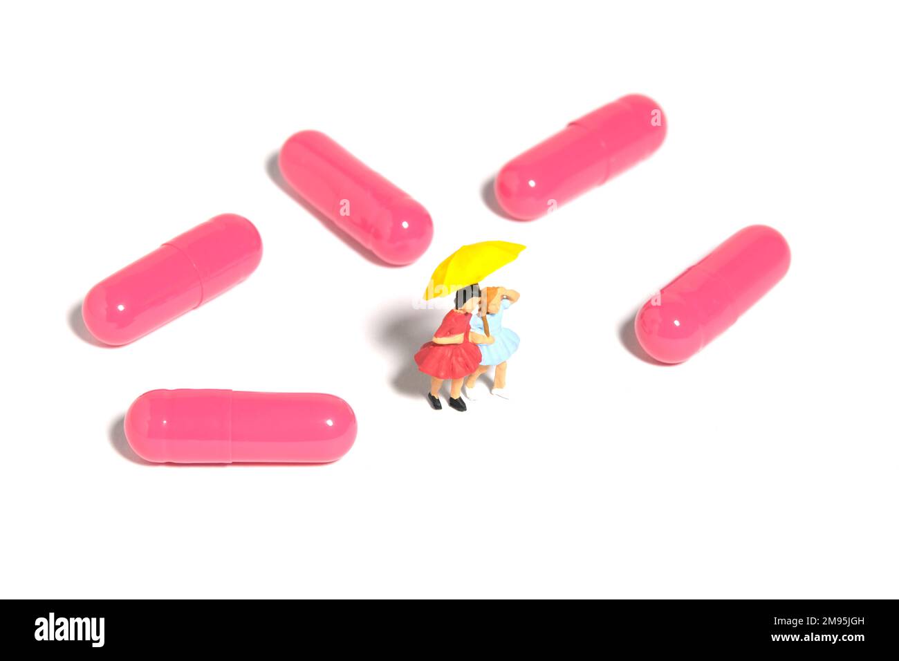 Fotografia di figura giocattolo delle persone in miniatura. Due ragazze bambino in piedi in mezzo alla vitamina della pillola di droga rosa per il trattamento di influenza. Isolato su sfondo bianco Foto Stock