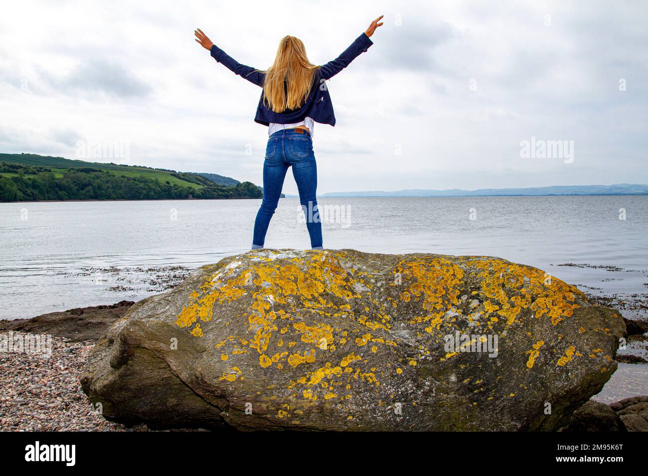 Rhianna Martin, una bella donna bionda, si erge sulle rocce mentre si gode il caldo tempo sulla spiaggia di Wormit nella contea di Fife, Scozia, Regno Unito Foto Stock