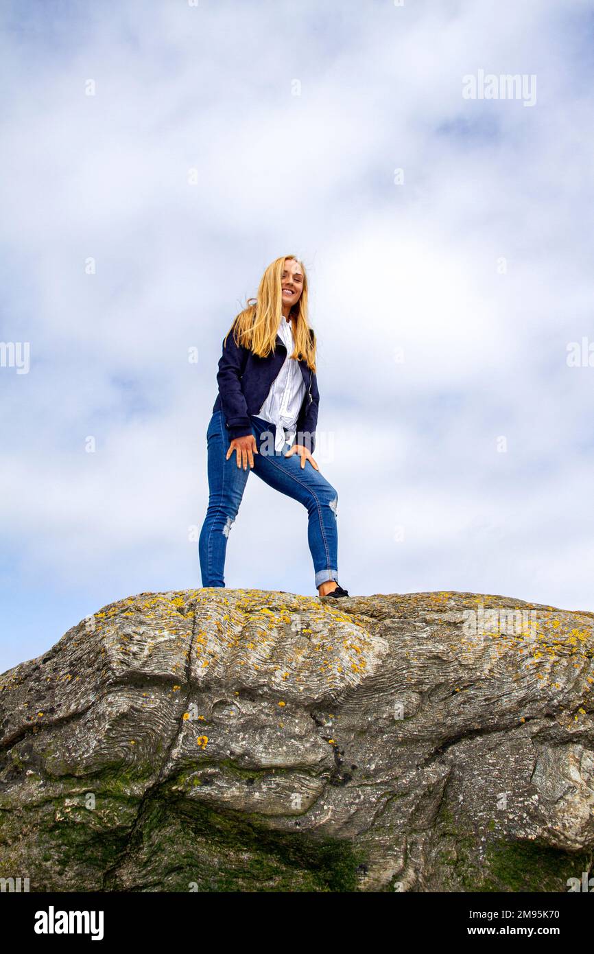 Rhianna Martin, una bella donna bionda, si erge sulle rocce mentre si gode il caldo tempo sulla spiaggia di Wormit nella contea di Fife, Scozia, Regno Unito Foto Stock