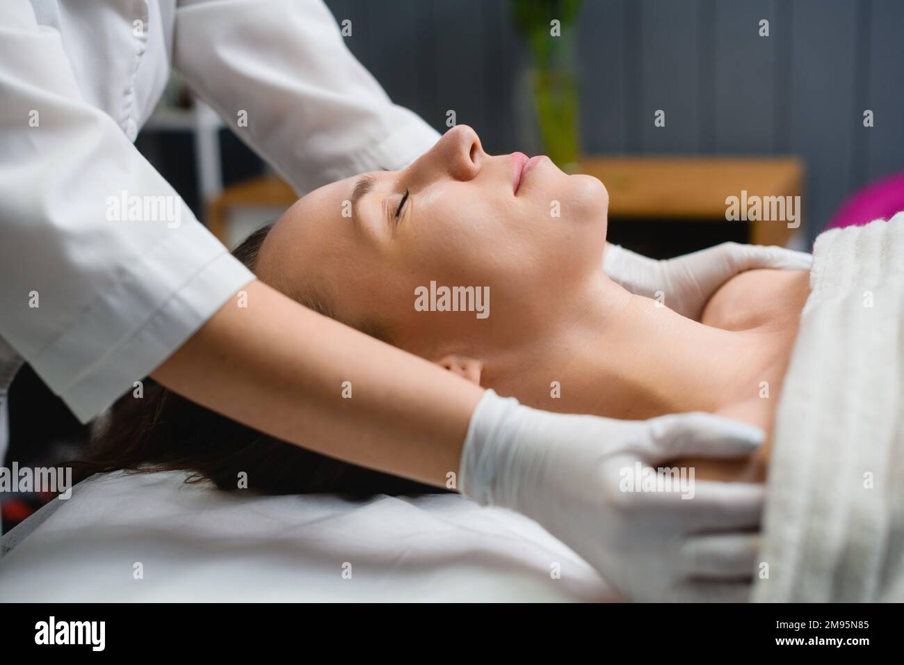 Massaggio cosmetologico viso, scollo e spalle in salone, mani massaggiatrice in guanto protettivo relax cliente, vista laterale Foto Stock