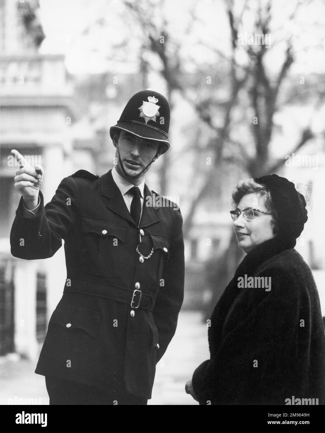 Un giovane poliziotto amichevole indica una donna di mezza età nella giusta direzione. Foto Stock